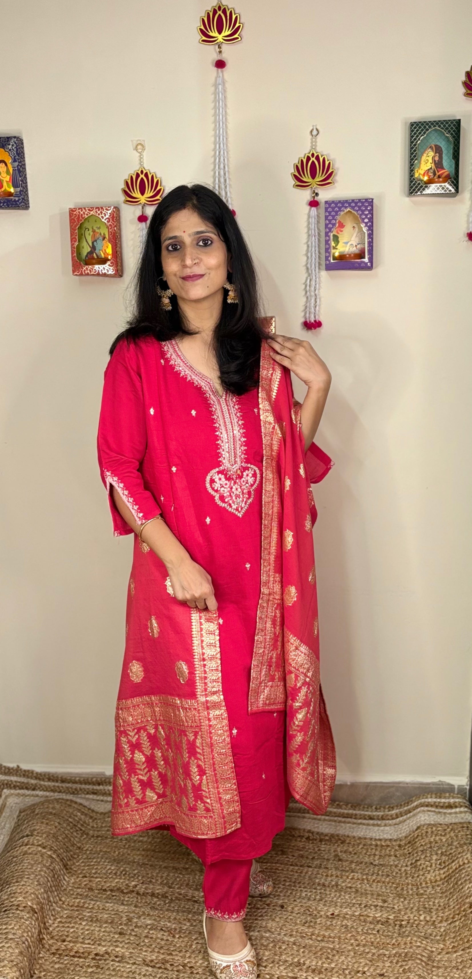 Woman in a pink traditional feeding or nusrsing  outfit standing in a room with decorative items on the wall.